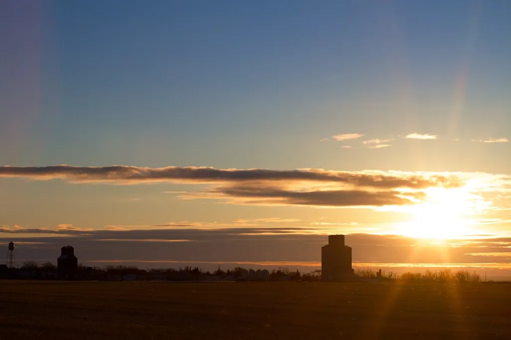 Grain silos silhouetted on a flat horizon at sunset